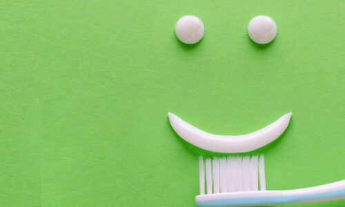 auf einem hellgrünen hintergrund ist aus zahnpasta ein smiley mit zwei weißen augen und einem weißen lächeln zu sehen.