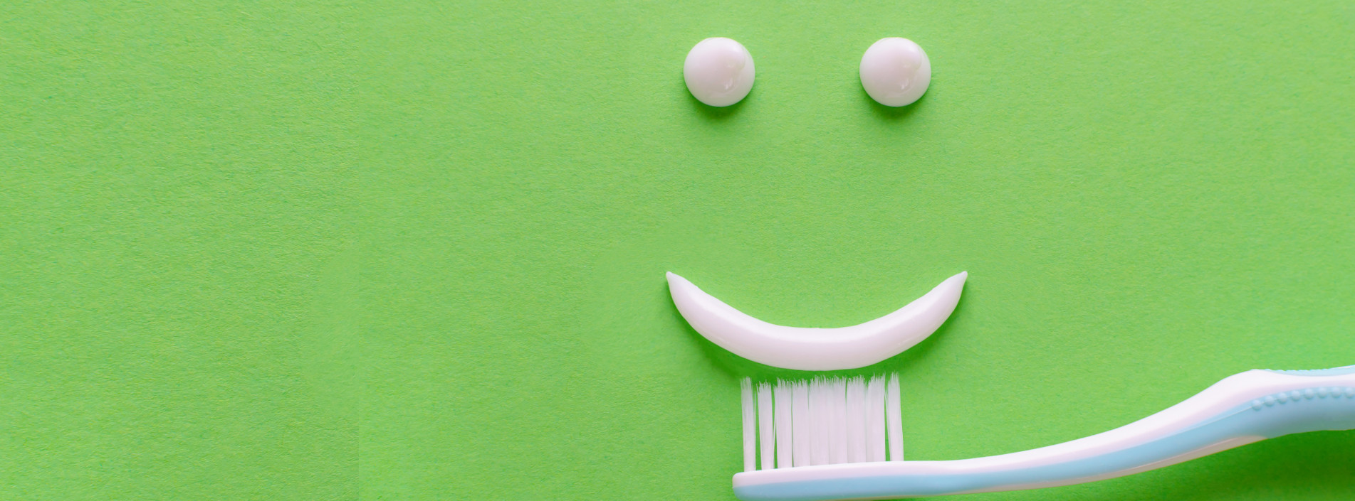 auf einem hellgrünen hintergrund ist aus zahnpasta ein smiley mit zwei weißen augen und einem weißen lächeln zu sehen.