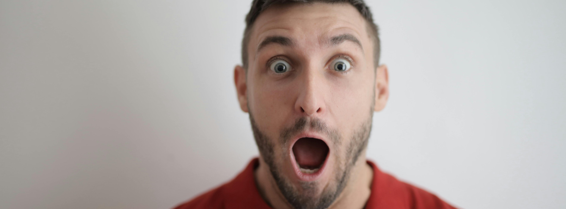 junger mann mit kurzen haaren und dreitagebart ist überrascht und öffnet augen und mund weit